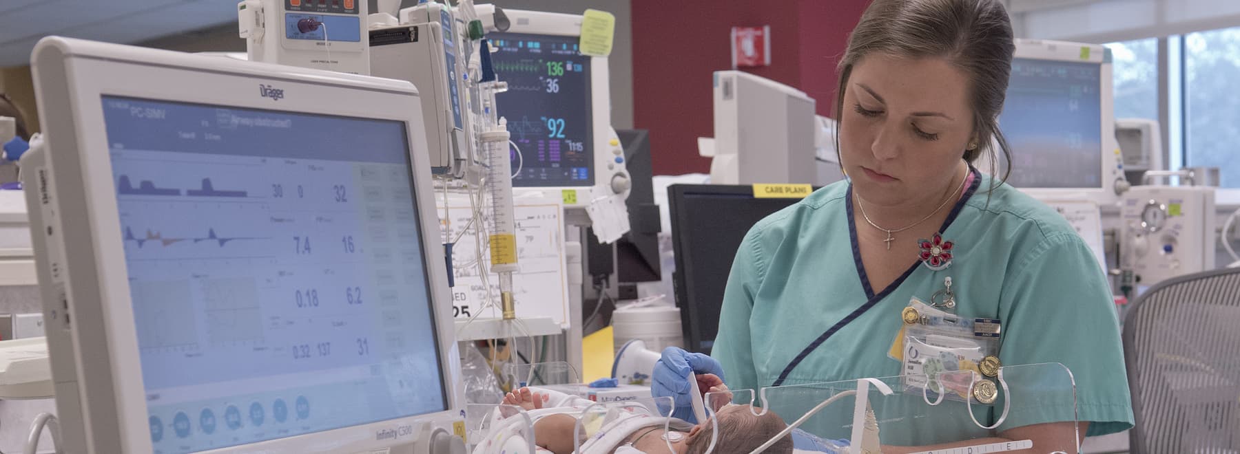 NICU nurse tending to newborn patient. Vital signs monitor is to the left.